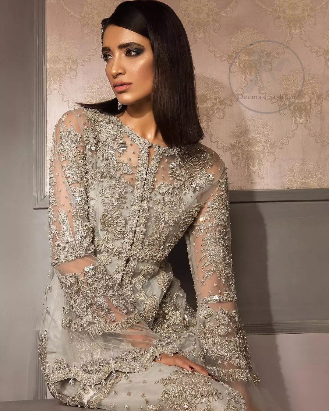 This beautiful gown is decorated with resham thread, kora, dabka, tilla, sequins and pearls. It is sculptured with floral thread embroidery. Sleeves are bell shaped and fully embroidered. It comes with brocade straight trouser. It is beautifully coordinated with organza dupatta.