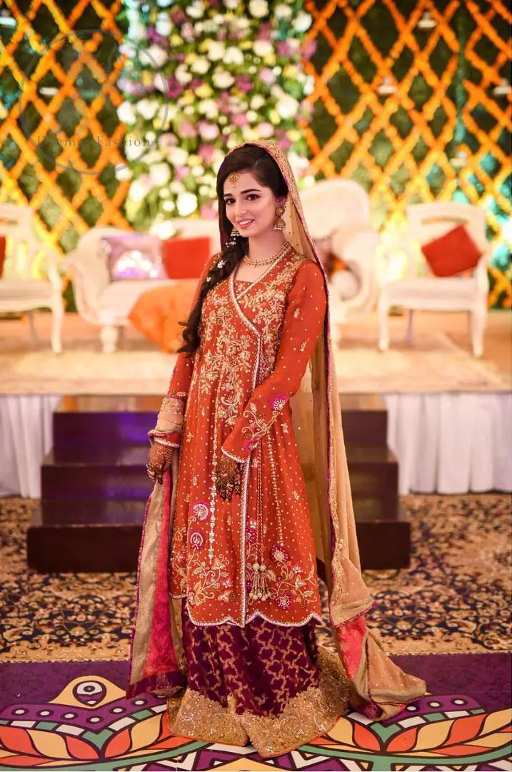 This outstanding outfit is fully embellished with embroidery. It is allured with resham, kora dabka, tilla and pearls. Sleeves are decorated with floral embroidery. Its neckline and hemline is adorned with floral motifs.It comes with embellished sharara which has small sized sprinkled floral motifs at the bottom. This Outfit is beautifully coordinated with dull yellow dupatta with heavy embroidered borders.