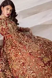 The grand maroon bridal stands out due to its uniqueness and the perfect fusion of modern cut and traditional embroidery. This halter neckline maxi is done with heavy embellishment of golden kora dabka, kundan, tilla, pearls and sequins work. It is further ornamented with detailed floral motifs. It is coordinated with brocade churidar pajama.