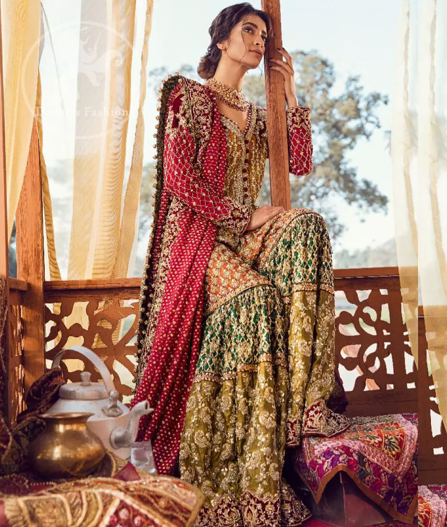 Exquisite detailing radiates elegance in this stunning short shirt. Redefine your style in this traditional and versatile ensemble ornamented with floral and geometric embroidery furnished with golden kora dabka, kundan and pearls. It comes with multiple colored traditional gharara done with zerdozi work in patterns and embroidered applique details on bottom. Complete the look with red dupatta having embroidered borders on all sides and sequins spray on the ground.