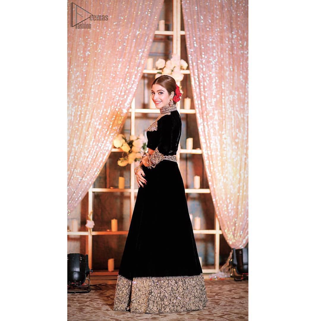 Embrace the season of festivities with this beautiful dress. This elegant ensemble turns timeless piece into a chic fantasy. The halter neck blouse is delicately hand crafted using the finest old age techniques and materials including kora, dabka, tilla, sequins, stones, and crystal. The sleeves are embellished with a thick embroidered border. Lehenga comprises of thick embroidered bottom to give it a regal look. It comes with a black net dupatta with sequins sprayed all over it .