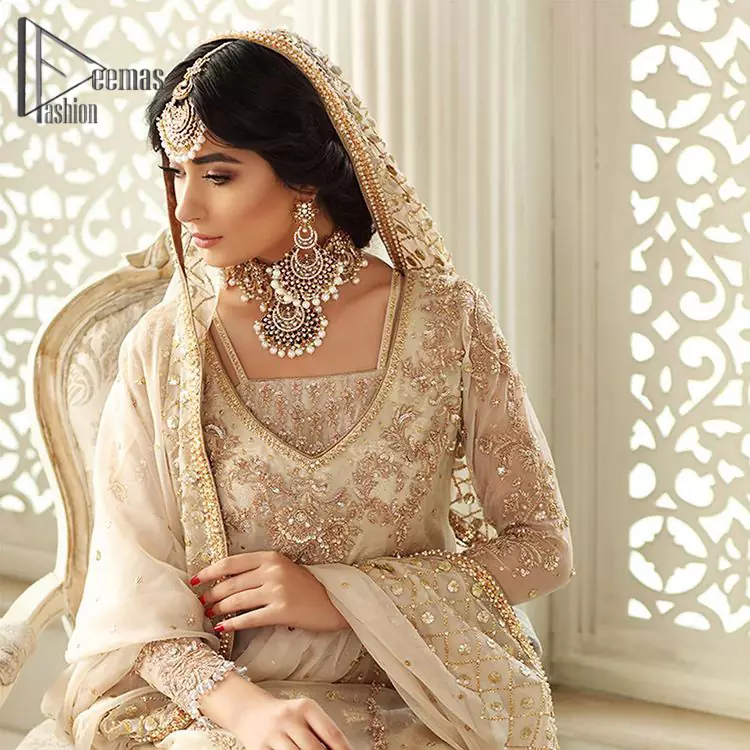 Pure bliss is seeing a bride smiling ear to ear through her whole wedding. Just go with a retro vibe on your Nikkah, everyone call you super queen. This ivory long shirt is pleasingly furnished with golden and antique embroidery that includes kora, dabka, tilla, and crystal work. The blouse is intensified with a V neckline just to give you a super surprising look. It is systemized with ivory sharara that border is embellished with beautiful embroidery as well. Complete this amazing look with a dupatta which is adorned with a four-sided handsome border and sequins spray all over with so much love.