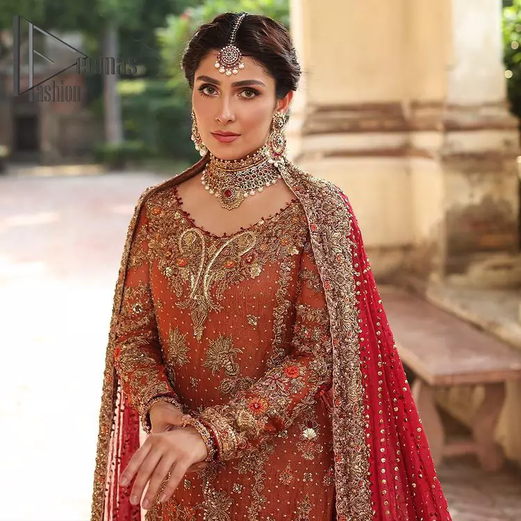 Wondering what an aesthetic bridal attire looks like? The beauty in red makes you go gaga over your look and you cannot stop snowing over you. Wearing the rust long shirt on your big day that is marvelously adorned with kora, dabka, and sequins work. Furthermore, the round neckline is also beautifully decorated to enhance the beauty of the outfit. It is synchronized with a red lehenga that has sequins sprayed all over to give you a crazy look as well. Finish this look with a red dupatta that has four-sided embellished lace as well.