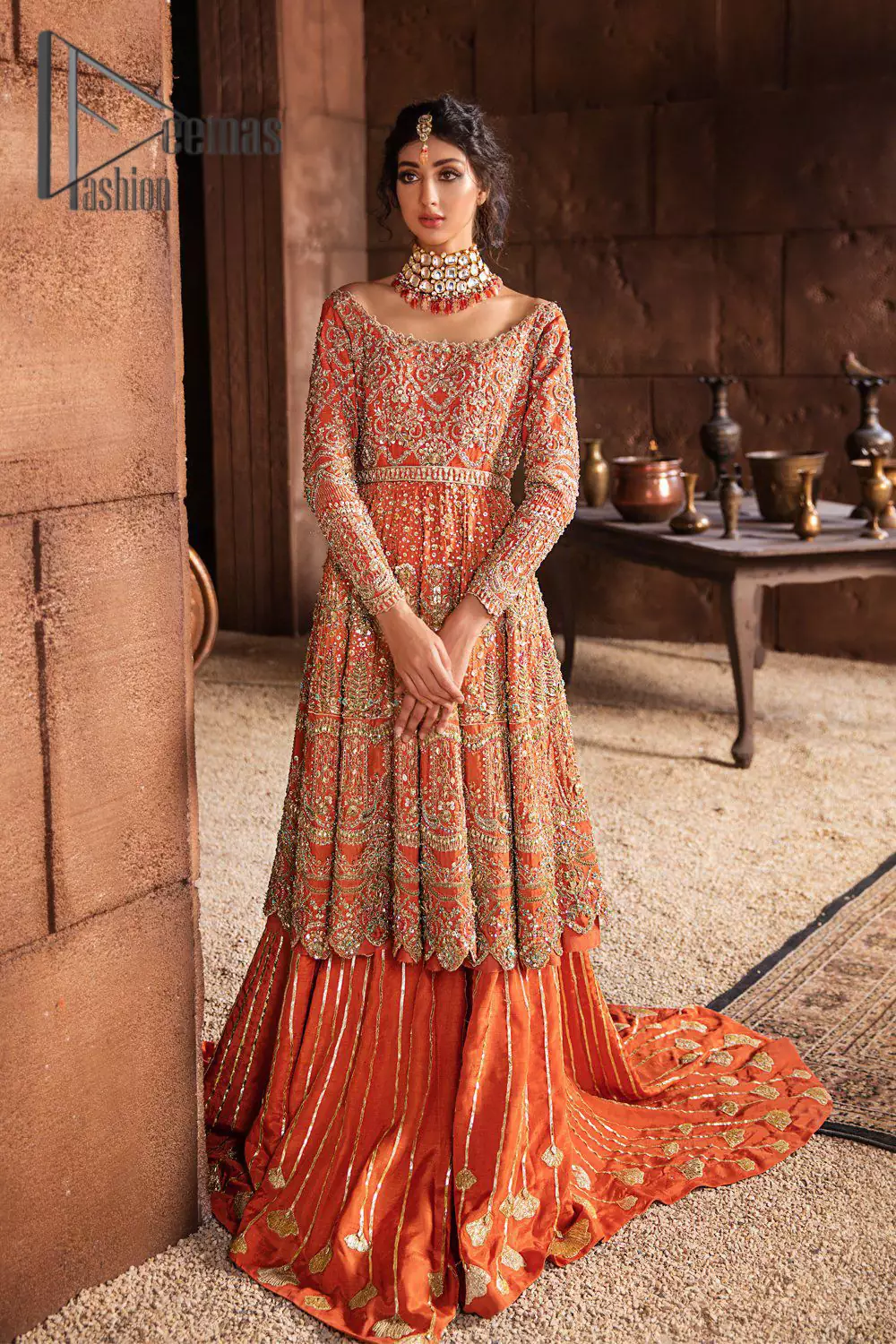 Fall in love with elements of detailing. Embrace your Mehandi style story with this orange attire serving vogue at its best. This orange frock is attractively adorned with golden embroidery that is further highlighted with kora, dabka, tilla, and antique work. And the scalloped border of the frock is just amazing so you can steal everyone's heart. In addition to this when the boat shape neckline combines with full sleeves it gives a super aesthetic scene. It is beautifully paired up with back train sharara that makes you a focus star of the day.