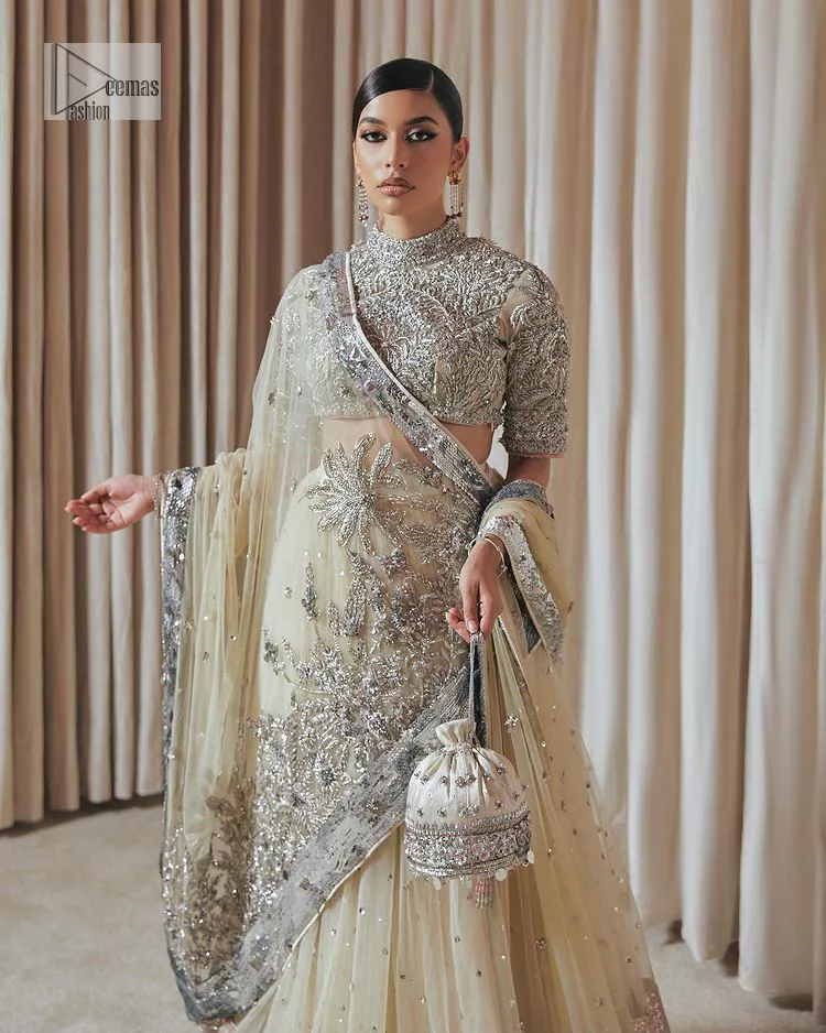 The perfect balance of simplicity and flamboyance is the essence of the beautiful Walima outfit. The blouse in off-white colour is beautifully embellished with Dabka, Tilla, Zardozi and delicate yet intricate crystal work. The beautiful classy artistic half sleeves design maintains the charm of this blouse. The beautiful outfit is epitome of beauty by its high neckline . It is paired up with flared lehenga in the same colour, framed with a sequins sprayed all over. Further, beautiful silver embroidery on the four sided border of the dupatta will enhance the overall magnificent look.