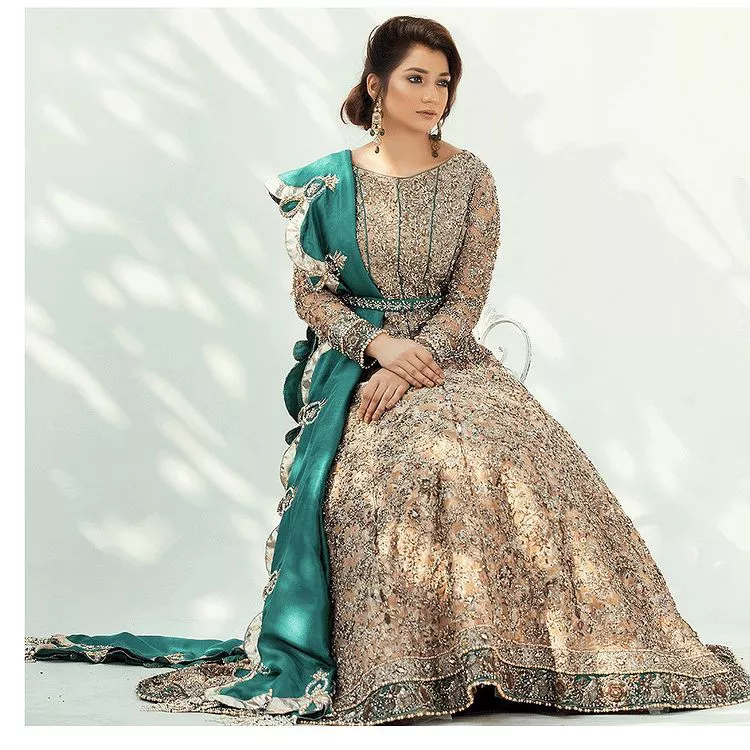 Celebrate your party with a bang and steal everyone's heart. The beautiful blouse in teal green shade comes in organza fabric. The boat shape neckline and full sleeves of this organza blouse are emblazoned with luxury details and intricate designs. Graceful golden embroidery that enhances with tilla, dabka, kora, Kundan, Zardozi and crystals to give a perfect finishing look to the blouse. It is organized with a back train lehenga which is heavily adorned with embroidery to make this masterpiece super aesthetic. Finish this outfit with a scalloped dupatta having four-sided embellished borders for a fine finishing look.