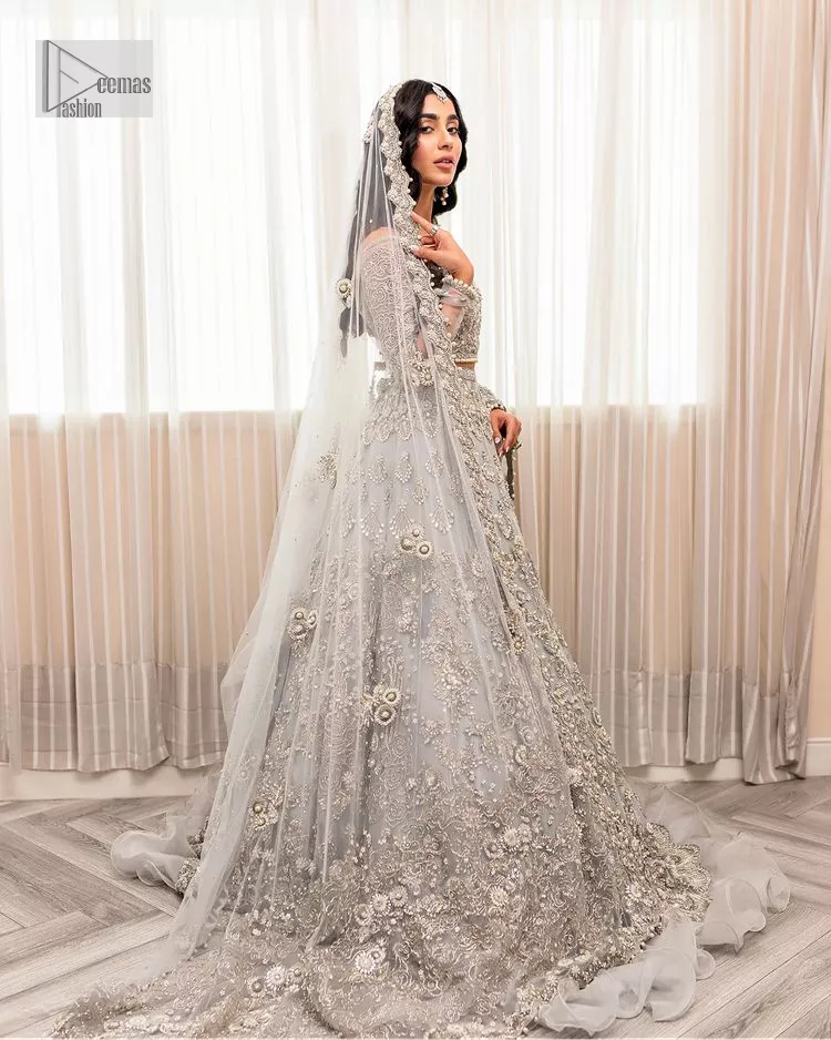 Enter the world of allurement with steel grey, a gorgeous go-to dress for nikah to make you look classy and fabulous at the same time! The delicate details of this gorgeous bridal dress are from exquisite patterns observed in silver embroidery which is prominent with tilla, dabka, kora, Kundan, Zardozi and the real magic of crystals. The house has V shape neckline to make this masterpiece a little romantic and classy. Further, full sleeves are fully designed with fantastic floral patterns spread all over. It is paired with a lehenga having frilled to complete the lavish look of this fully embellished nikah wear. Complete this article with a dupatta adorned with four-sided embellished borders and sequins sprayed all over.