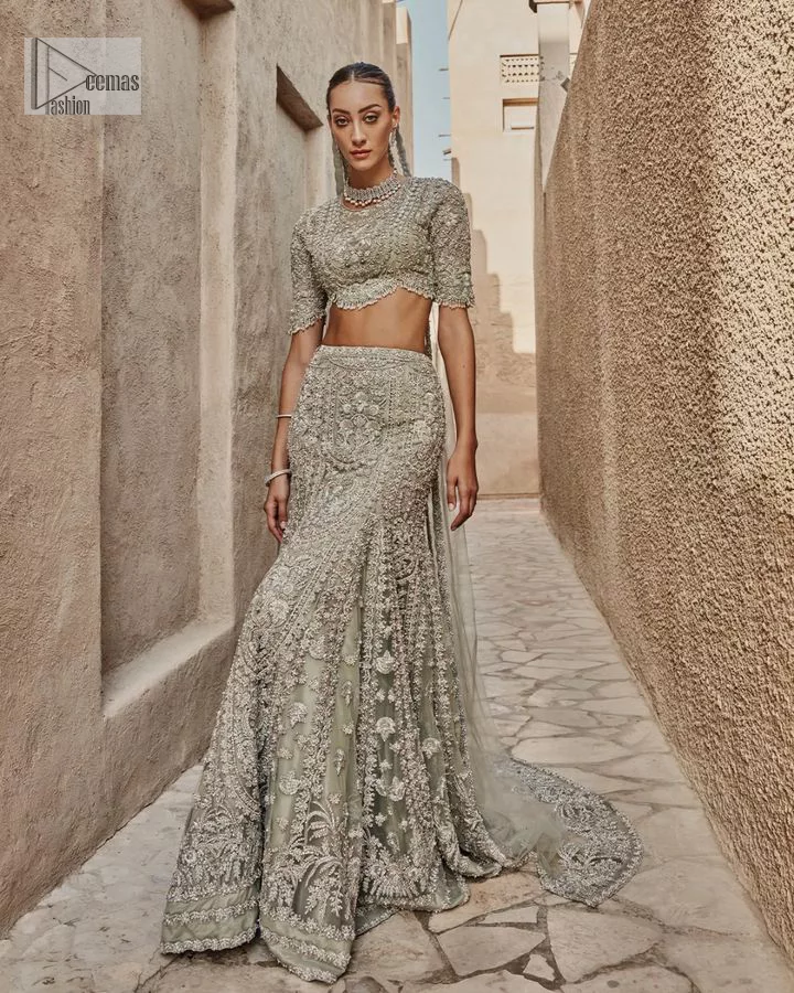 This fusion of floral embroidery is total fashion goodness for a walima outfit! A stunning teal grey organza choli embellished with intricate detailing finished with a scalloped border. The beautiful blouse is decorated with silver embellishment which is further prominent with tilla,daka, kora, Kundan and the real magic of Zardozi.  It is paired with a heavily embellished back-train lehenga with botanical motifs and geometric patterns. Its dupatta is made from a net. The dupatta is a wide embellished border that added divine charm to the entire ensemble.
